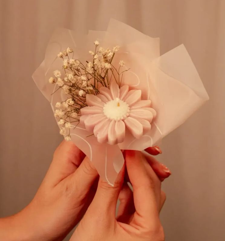 Manos sosteniendo una flor de cera envuelta con flor seca