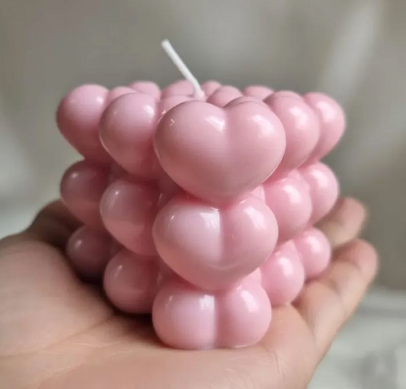 Vela decorativa de corazones rosa en la palma de una mano